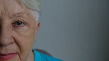 Close up portrait of beautiful older woman smiling and standing by wall with gray eyes.