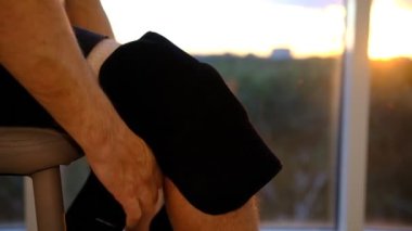 close up of knee support brace on leg of a man in sunset lights near the window.