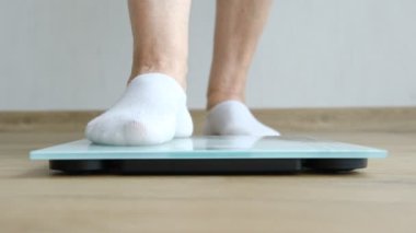 old woman standing on weight scale in living room, senior woman cheking her weight on digital scales.