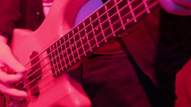 Rock müzisyeninin elleri kırmızı ışıkta tekrar eden elektro bas gitar çalıyor..