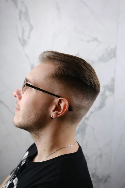 Male beauty concept. Portrait of fashionable young man with stylish haircut wearing trendy glasses and tshirt, posing over gray background. Perfect hair. Copy-space. Studio shot.