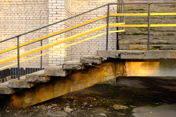 old concrete steps with yellow metal railings leading in to the building.