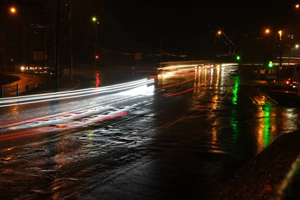 Lights of cars at night. Street lights. Night city. Long-exposure photograph night road. Colored bands of light on the road. Wet road after rain