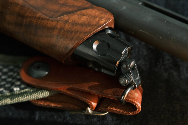 оболочка магазина в ствол длинного дробовика на темном фоне с кожаным ремнем.