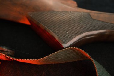 Closeup of a wooden shotgun butt. Hunting semi-automatic shotgun with a wooden button dark background with red light.