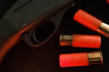 Siyah arka planda bir tüfeğin tetikleyicisi. Üzerinde siyah bir yüzey üzerinde Shotgun fişekleri olan kırmızı bir yıldırım. 12 kalibrelik pürüzsüz silahlar için mühimmat. Cephanelik avlıyorum. Koyu arkaplan