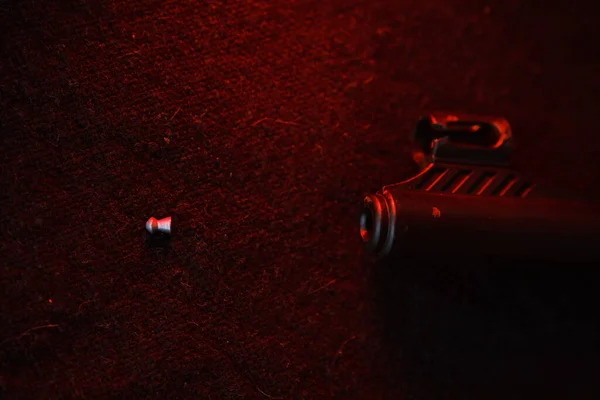 Rifle gun with air pellets for hunting on cloth dark background with red light illumination of the muzzle and pallet.