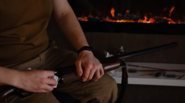 Tüfek temizleme tüfeği sökme işlemini başlat. Bahar av sezonunun açılışı. Bir adam tüfekle nişan alıp avlanmadan önce bakım yapar. Arka planda şömine olan elleri kapatın..