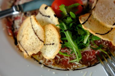 Parmesanlı, domatesli ve roka soslu, koyu renk etiketli Carpaccio bifteği..