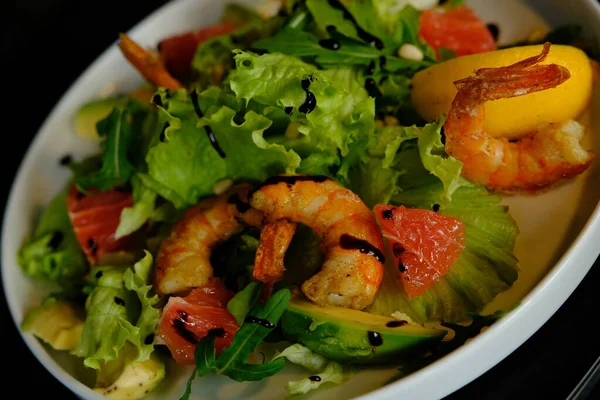 Shrimp and avocado salad in white plate with tomato and lemon.