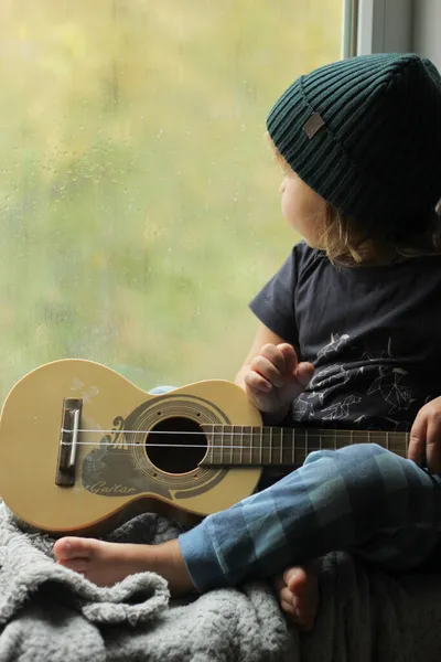 Gitarlı bir çocuk pencere eşiğinde oturur ve pencereden dışarı bakar. Sonbahar yağmurlu günü