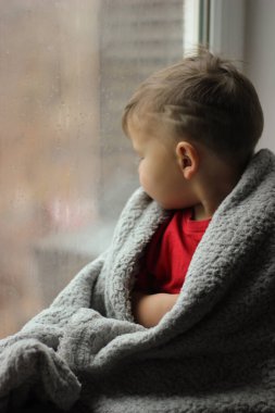 Bir çocuk pencereden dışarı bakıyor. Beklenti, çocuk güvenliği ve plastik pencereler kavramı.