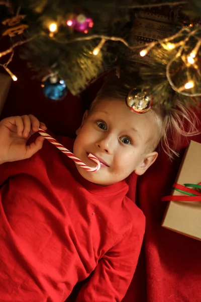 beautiful boy whith blond hair in red T-shirts lie. Cute boy with lollipop look at camera. sweet red candy on a stick. top view