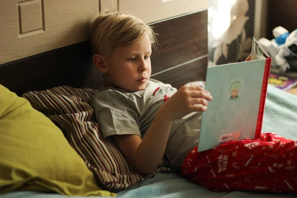 bir kitapla yatakta yatan çocuk. Çocuk okuma