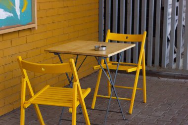 Sarı ahşap kafe masası ve dışarıda beyaz sandalyeler..