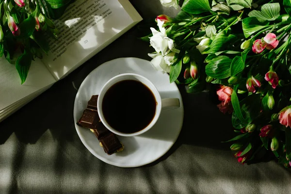 Yatakta kahve, romantik bir sabah. Çiçekler, açık bir kitap ve tahta tepside bir fincan kahve. Ev içi rahat, yaşam tarzı. Seçici odak