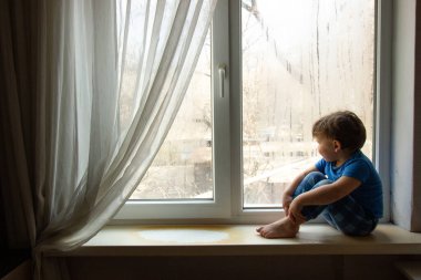 Küçük bebek pencere kenarında oturuyor ve dışarı bakıyor ve gülümsüyor. Pencerede yaşam tarzı portresi.