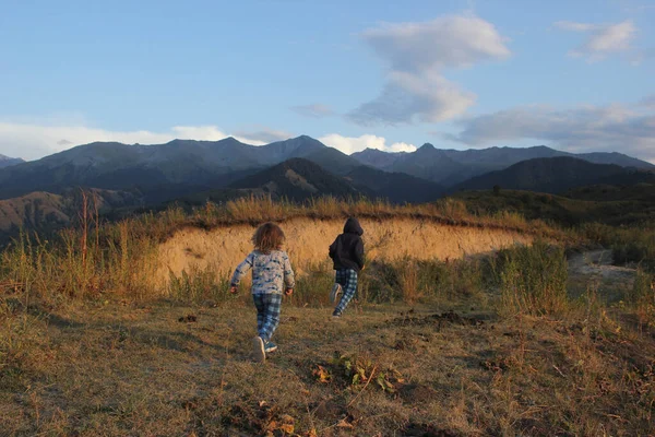 Bir çocuk yaz mevsiminde dağların arka planına doğru mutlu bir şekilde koşar.