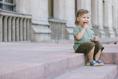 Küçük çocuk merdivenlerde lolipop yiyor. Yaz güneşli bir gün