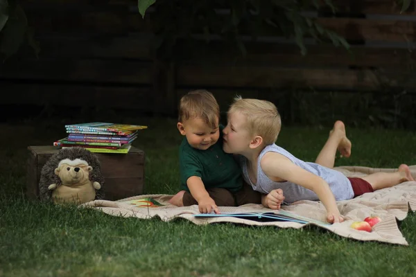 İki neşeli çocuğun dijital tablet kullanan geniş açılı portresi parktaki yeşil çimlerin üzerinde güneş ışığıyla aydınlatılmış olarak yatıyor.
