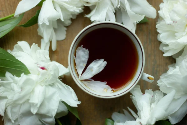 Ahşap arka planda çiçek desenli beyaz seramik bardak. Çiçek çayı konsepti.