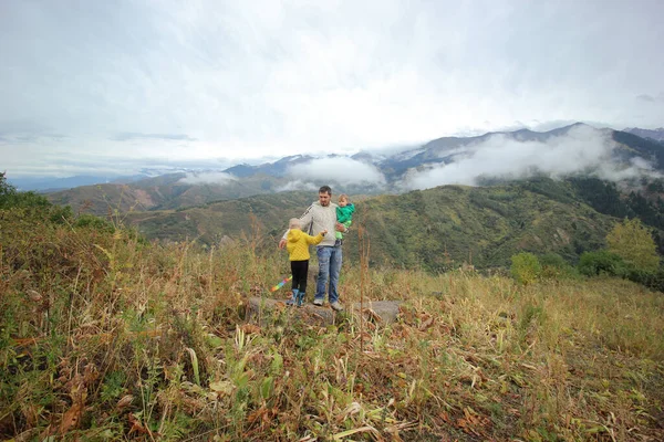 Babası ve çocuğu dağda yürüyüş yapıyor. Genç turistler dağın tepesinde manzaranın tadını çıkarıyorlar. Mutlu bir aile. Babam ve güneş. Tatil gezisi konsepti. Dünya Turizm Günü. Arka plan