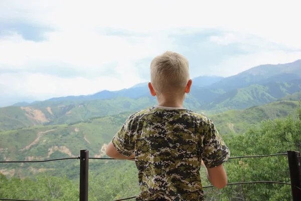 Erkek turist bir dağ evinin terasında duruyor ve bulutlu dağ manzarasına bakıyor.