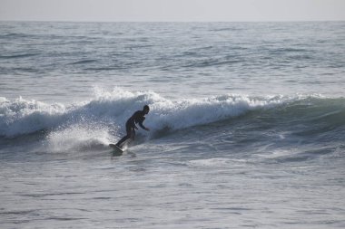 Siyah mayolu genç adam ve deniz kıyısındaki dalgalar içinde siyah sörf tahtası..