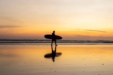 Surfer on the beach at sunset. Surf silhouette of man walking with surfboard at golden hour beautiful colors