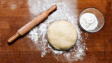 Ahşap zemin üzerinde un tozu olan bir hamur topu. Masada merdane, un ve hamur var. Ev mutfağında pişirmek için çiğ taze hamur. Yumurtasız hamur. 