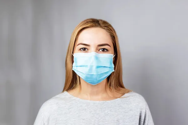 Virüs enfeksiyonunu durdur. Gri arka planda maskeli bir kız. Gri arka planda tıbbi koruyucu maskeli bir kız. Halka açık yerlerde virüslere ve mikroplara karşı koruma kavramı.