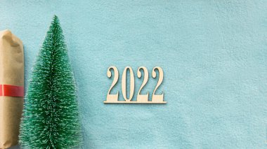 2022 numaralı ahşap, yanında bir Noel ağacı ve hediye kutusu bulunan mavi bir kumaş zemin üzerinde. Kopyala uzayı. Yeni yıl tebrik kartı. Yeni yılın numaraları 2022.. 