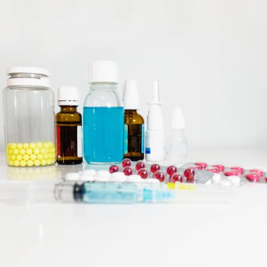 Arka planda tıbbi şurupların yanı sıra çeşitli damlalar, vitaminler ve ilaçlar yer almakta ve ön planda enjeksiyon için şırıngalar ve deffocus 'ta çeşitli tabletler, evde tedavi için antibiyotikler bulunmaktadır..