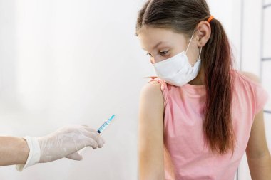 Aşı sırasında çocuk bir hemşirenin elinde aşı olan sürpriz bir enjektörle görünür. Yan görüş. Seçici odaklanma. Covid 19 virüsüne karşı çocukların aşılanması. Çocuklar için aşılar.