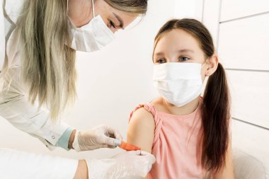 Lastik eldivenli ve koruyucu maskeli bir hemşire, çocukların aşılanması ve enjeksiyonlar için yakınlarda oturan bir çocuğun omzuna tıbbi sıvayı yapıştırıyor. Hastanedeki Doktor 'un resepsiyonundaki prosedürler..