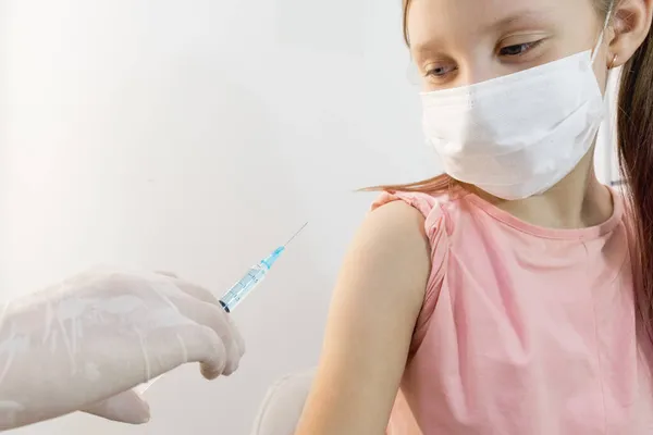 A child girl before vaccination looks at the needle of a syringe held by the hands of a nurse in medical gloves. Selective focus .Vaccinations for children. Treatment room. Syringe injections.Vaccination of children against the Covid 19 virus.