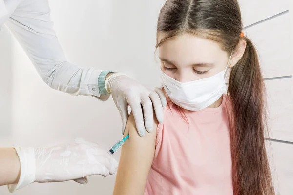 Bir hemşire bir kızın omzuna şırınga aşısı koyar. Seçici odaklanma. Covid 19 virüsüne karşı çocukların aşılanması. Çocukluk aşıları. Doktor 'un hastanedeki resepsiyonunda iğneler ve prosedürler.