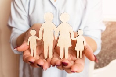 Dişi eller, bir ailenin tahta heykelini tutuyor. Seçici odaklanma. Aile yaratma ve planlama konsepti. Aile bakımı - ahşap silueti olan eller.