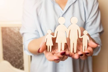 Dişi eller, bir ailenin tahta heykelini tutuyor. Seçici odaklanma. Aile yaratma ve planlama konsepti. Aile bakımı - ahşap silueti olan eller.