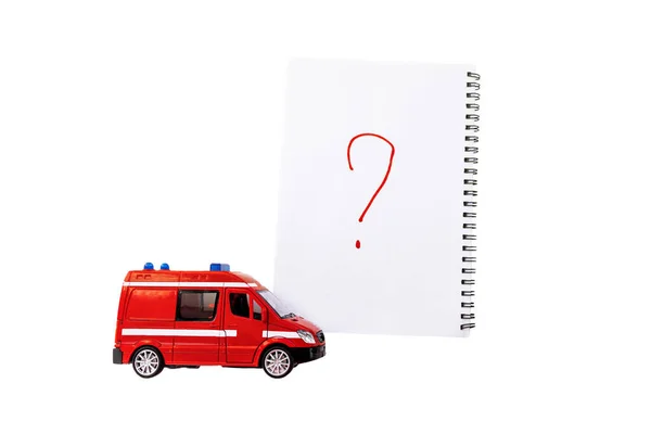 Üzerinde soru işareti olan bir not defterinin yanında oyuncak kırmızı bir ambulans ya da başka bir acil durum aracı. Beyaz arka planda izole edilmiş. Mesajın için yer. Acil durum. Program ve kurallar. acil taşıma