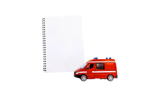 Oyuncak kırmızı bir ambulans ya da defterin yanındaki diğer acil durum aracı. Beyaz arka planda izole edilmiş. Mesajın için yer. Acil durum. Program ve kurallar. acil taşıma.