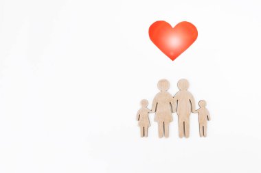 Beyaz arka planda tahta bir aile figürü ve kırmızı kalp sembolü. Seçici odaklanma. Ayrı bir nesne. Aile yaratma ve planlama konsepti. Dost canlısı bir ailenin ahşap silueti.