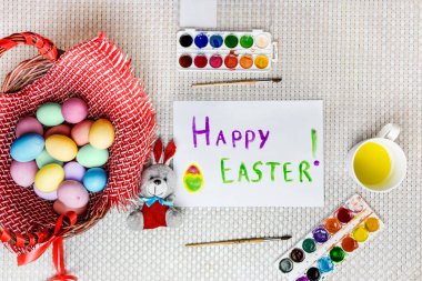 Boyalı Paskalya yumurtaları ve oyuncak bir tavşan pencerenin yanındaki ahşap bir sepetin üzerinde beyaz bir çarşafın yanında uzanıyorlar. Top View Mocup. Seçici odak ve beyaz arkaplan.