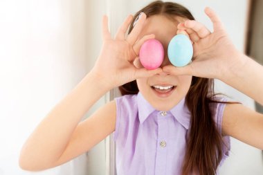 Çocuk kız gözlerinin yanında 2 Paskalya yumurtası tutuyor ve gülüyor. Seçici odaklanma. Uzayı kopyala. Doğuya. Çocuklar ve Paskalya yumurtaları