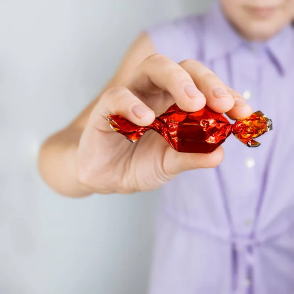 hand holds bright chocolate candy in a red wrapper. Selective focus. Blurred backgroundSweets and candies.