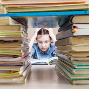 bored purposeful child reading a book studying grammar preparing for school and exams.reading books in the library. Stacks of books on a bookshelf. Exam preparation. Photo through bookshelf