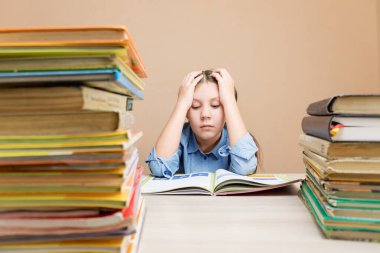 bored schoolgirl reading a book while sitting at a table with stacks of books with homework. Selective focus. bored purposeful child reading a book studying grammar preparing for school and exams.reading books in the library.
