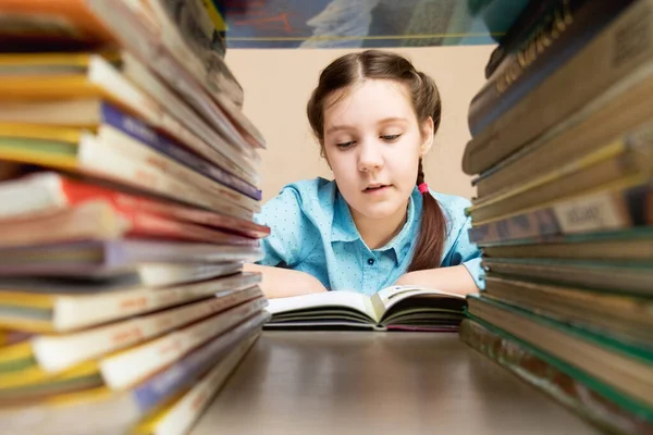 Girl child doing homework, reading a book, In the foreground are stacks of books on a bookshelf