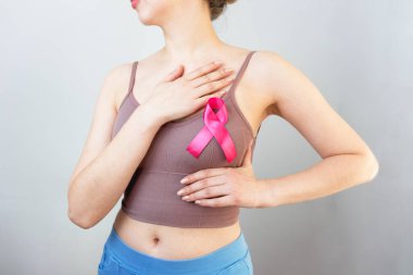 Dünya Göğüs Kanseri Günü. Göğüs kanserinin önlenmesi. Göğüs muayenesi. Bir kadın göğsü elle muayene eder. Dünya göğüs kanseri gününün sembolü olarak pembe kurdele. Kişiliğini kaybetme.