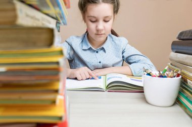 Öndeki masada yığınla kitap var. Arka planda, maksatlı bir çocuk kitap okur, okula geri döner, ödevlerini yapar, kitap okur..
